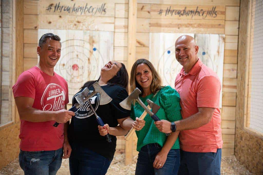Image of the couple owner along with another couple holding axes while posing for a picture at Throw Lumber Jills' axe-throwing lanes - www.throwlumberjills.com